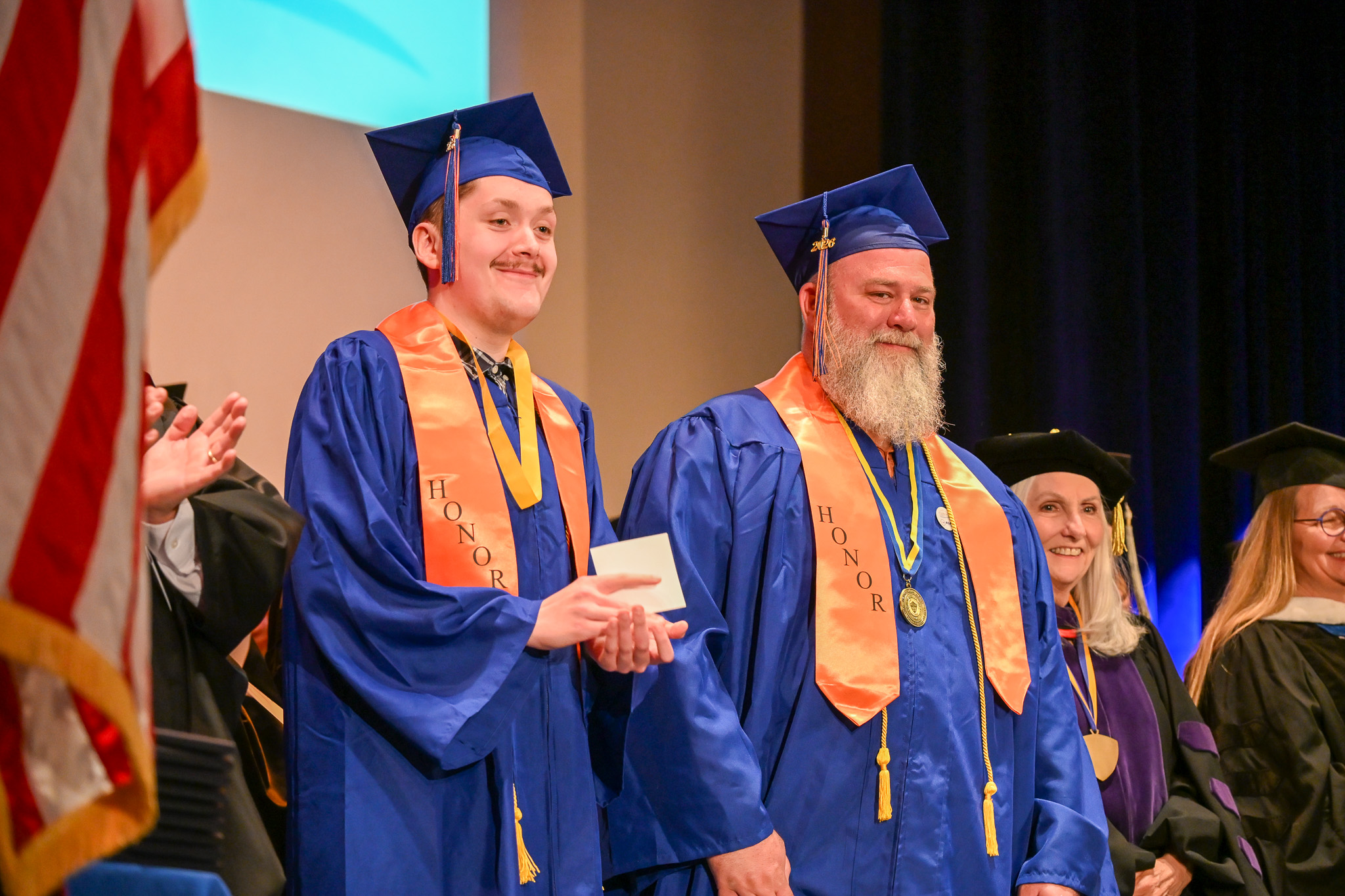 Two graduates wearing honors stoles on stage