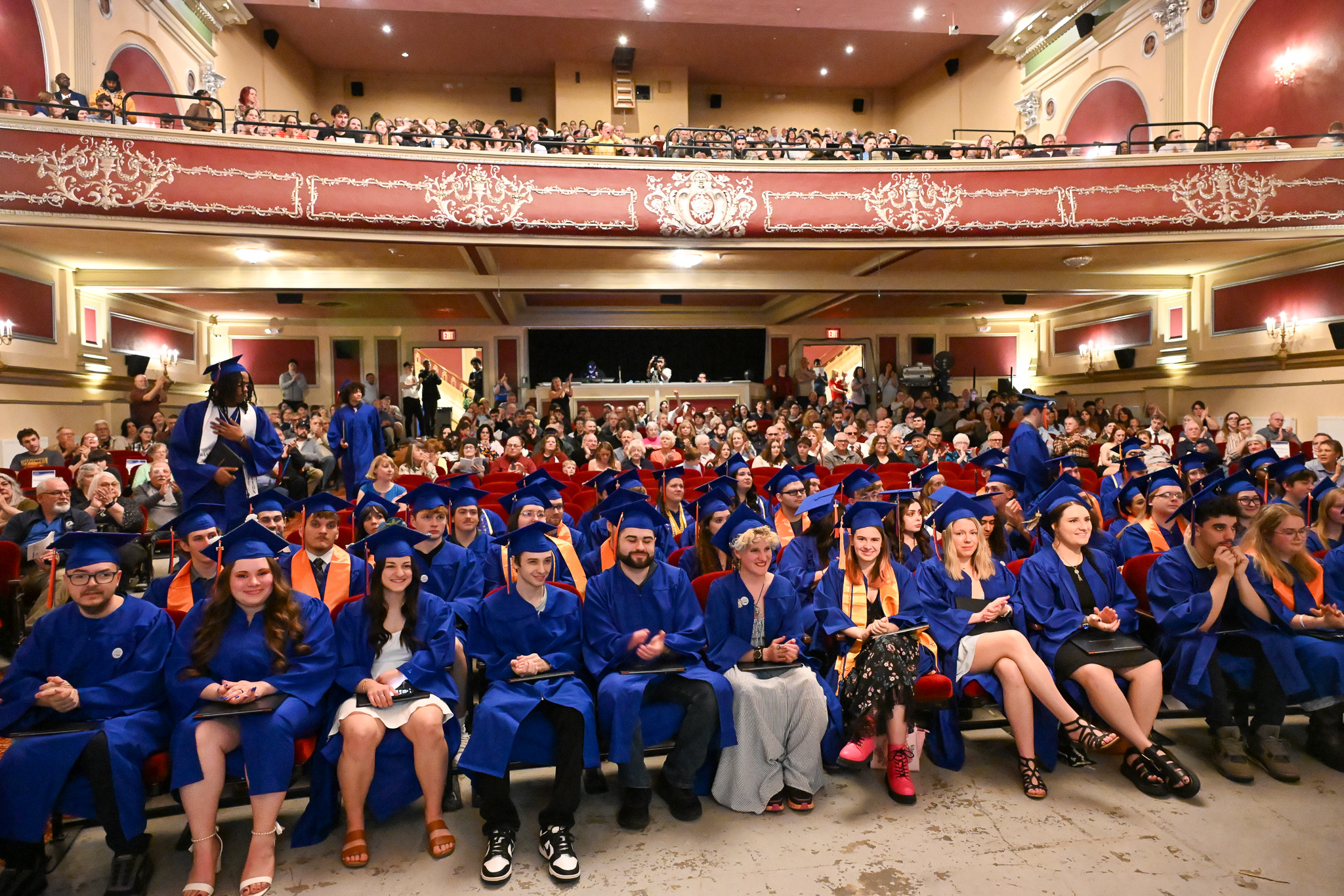 A group of dozens of people wearing graduation regalia in a packed theatre