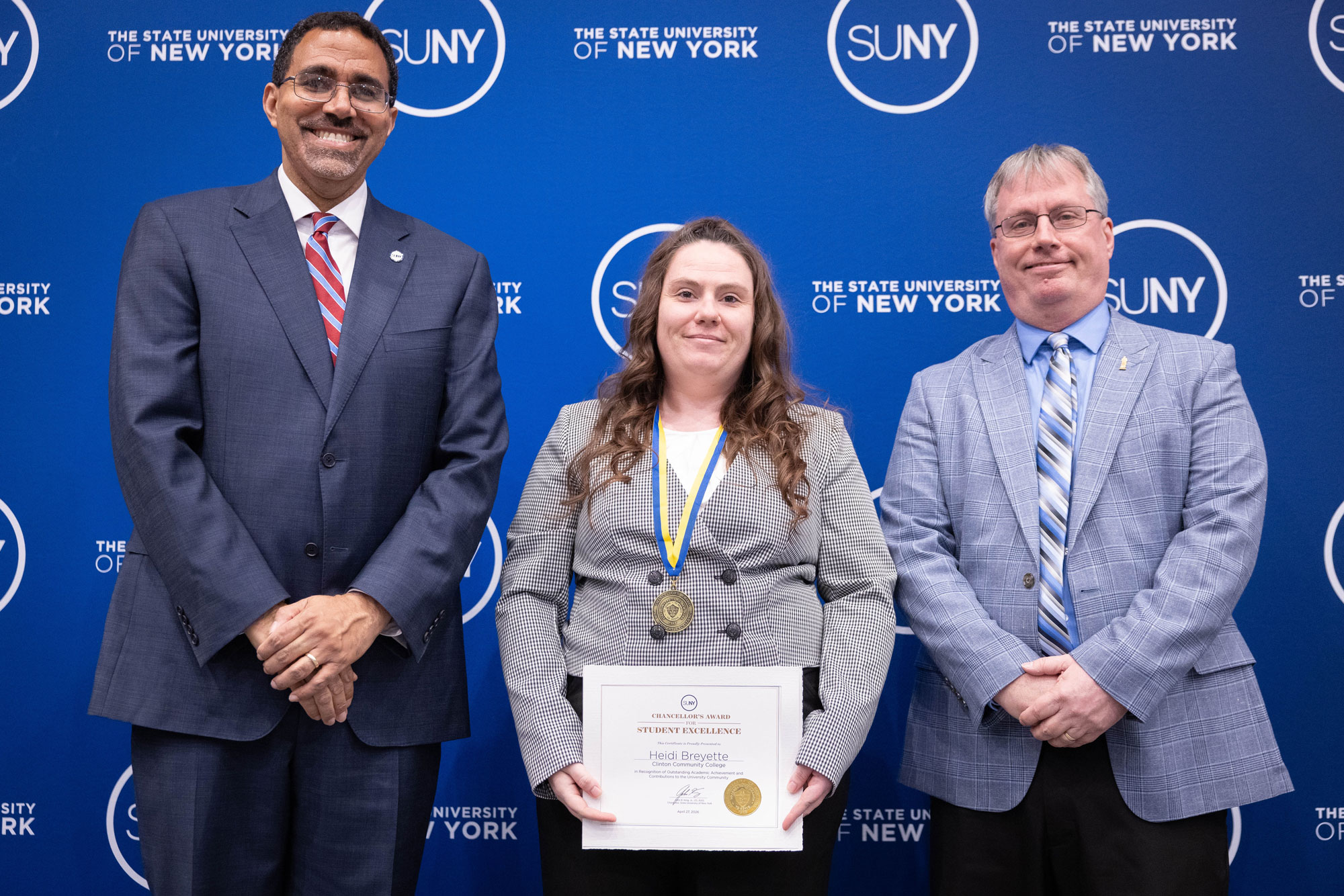 A person holding up an award while standing next to two other people in suits and ties