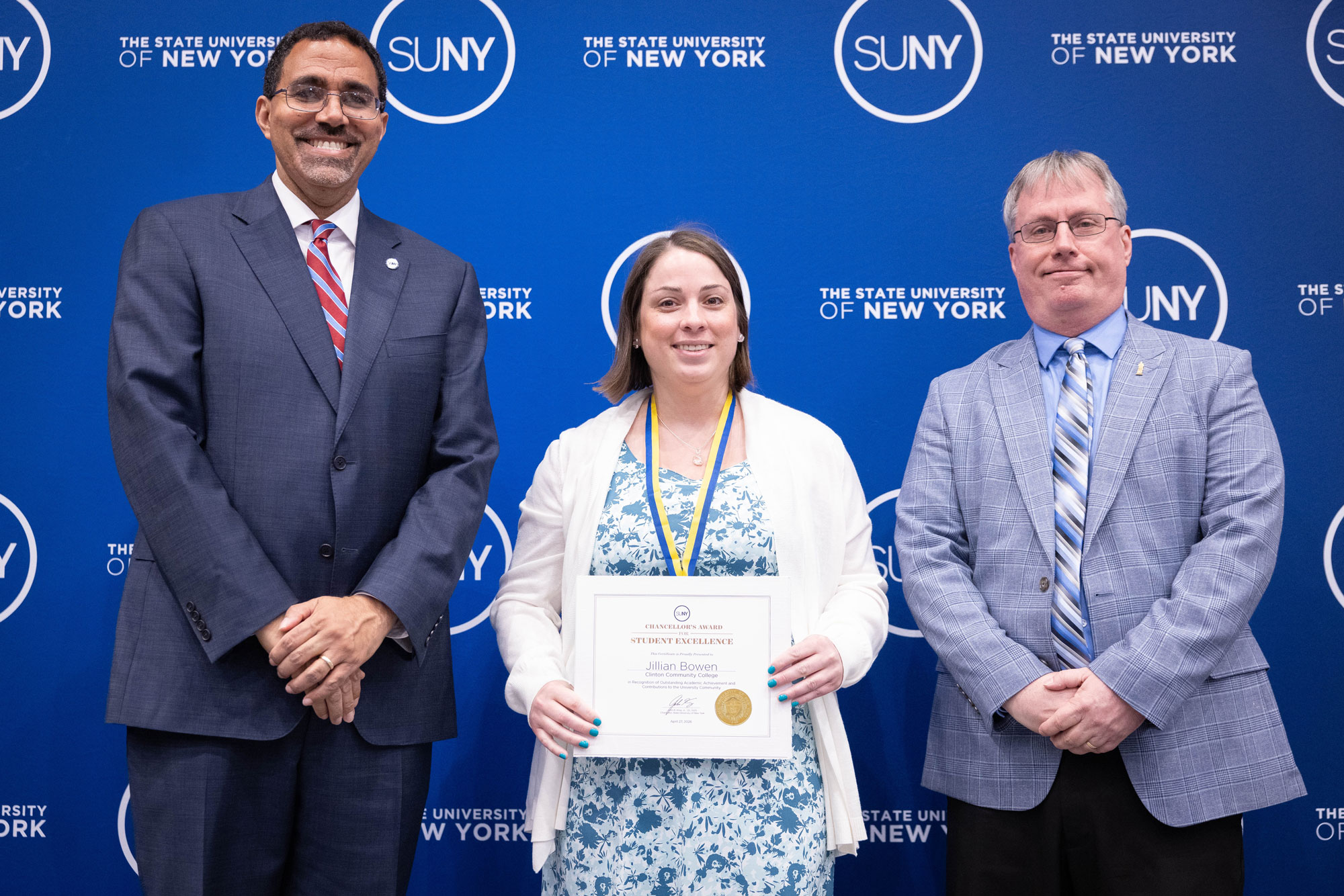 A person holding up an award while standing next to two other people in suits and ties