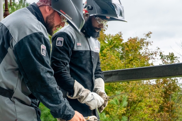 Two people in welding gear working on a project outdoors