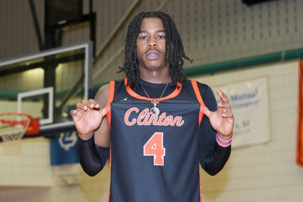 A basketball player holding their jersey that says 'Clinton 4' while inside a basketball arena