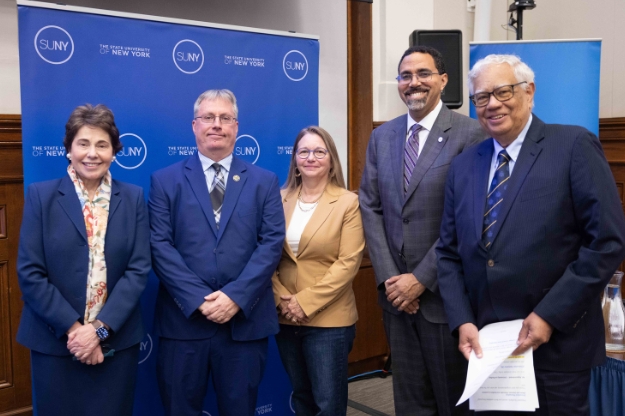Five people posing for a photo together in front of a blue backdrop with SUNY logos