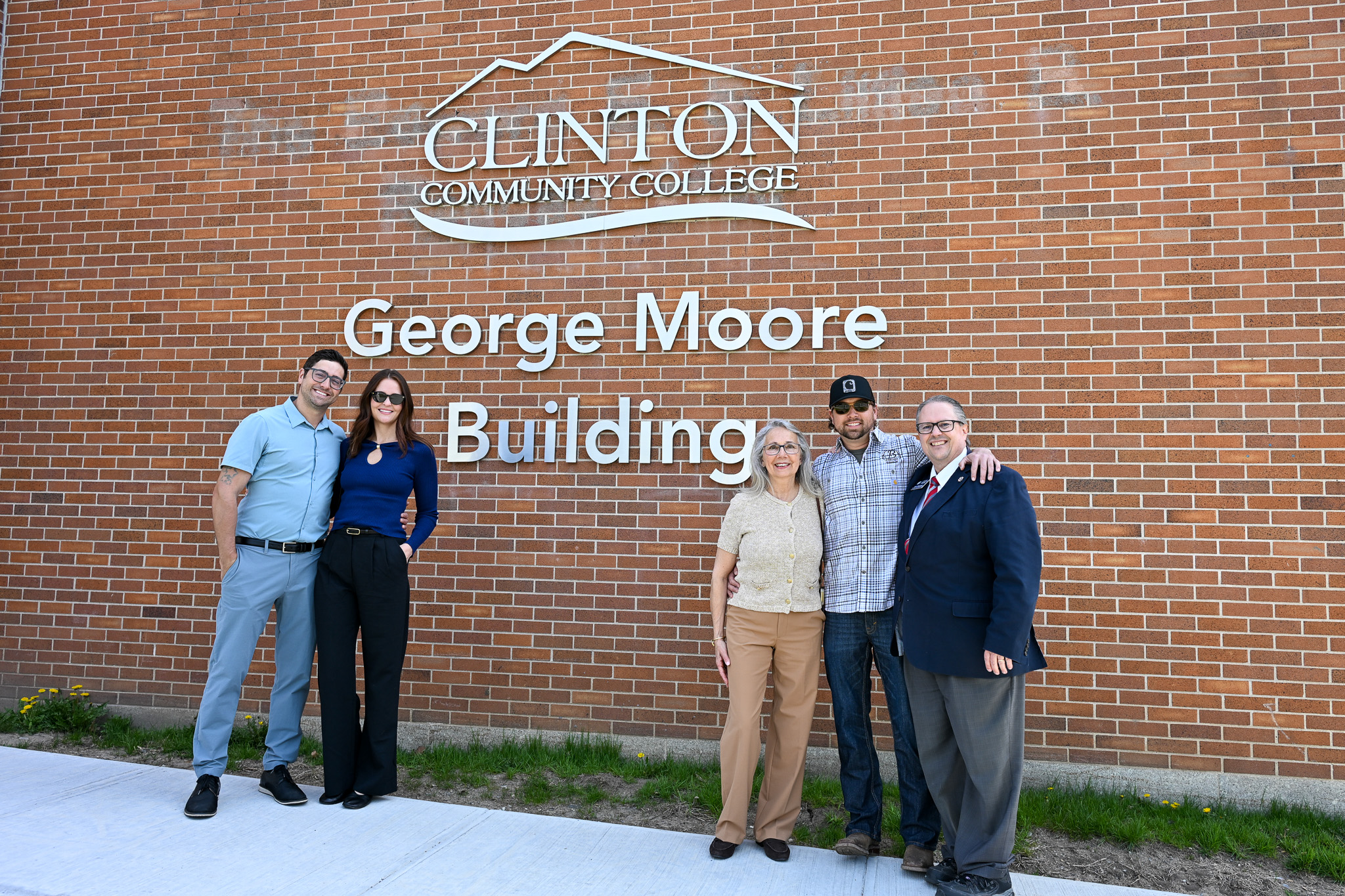 Four people standing near a sign that reads 'Clinton Community College George Moore Building'