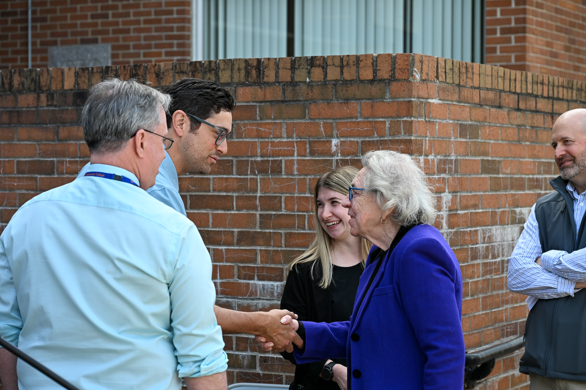 Two people shaking hands with others looking on nearby