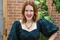 A person posing for a photo in front of a brick wall and green plant