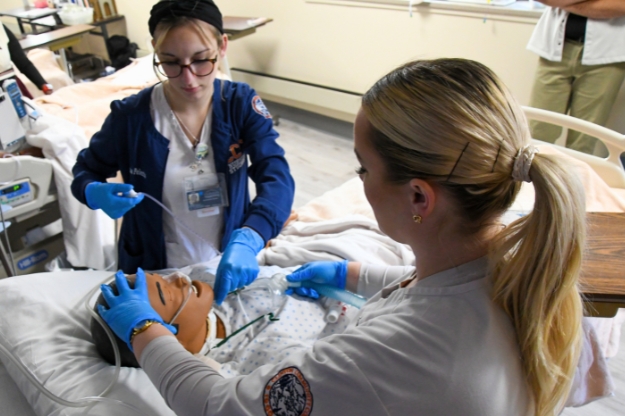 Two nursing students working on a mannequin patient in a hospital setting