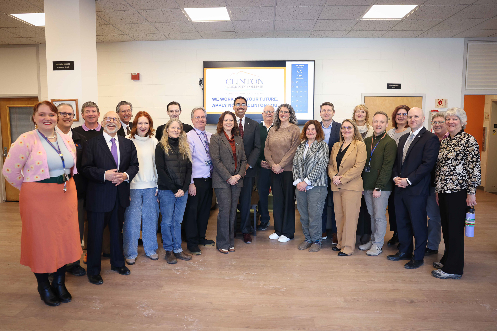 A group of people standing together for a photo in front of a monitor that reads 'Clinton Community College'